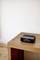 A black, rectangular radio sits on a wooden table in front of a white wall.