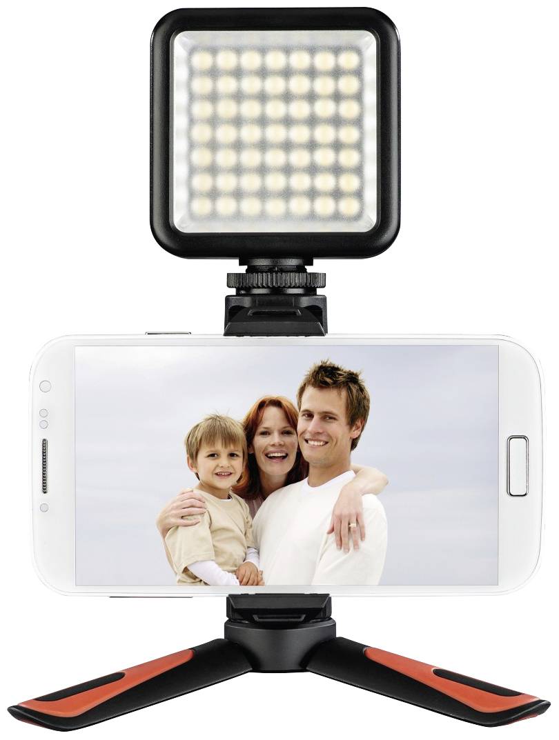 A family consisting of two adults and a child is smiling at the camera, depicted on a smartphone with LED light and tripod.