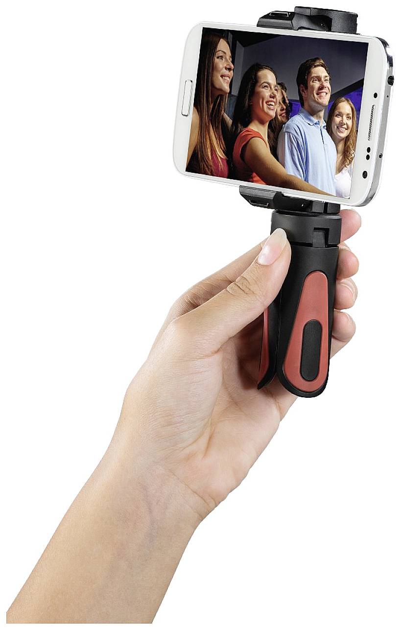 A hand is holding a smartphone with a selfie stick, and four people are smiling into the camera on the display.