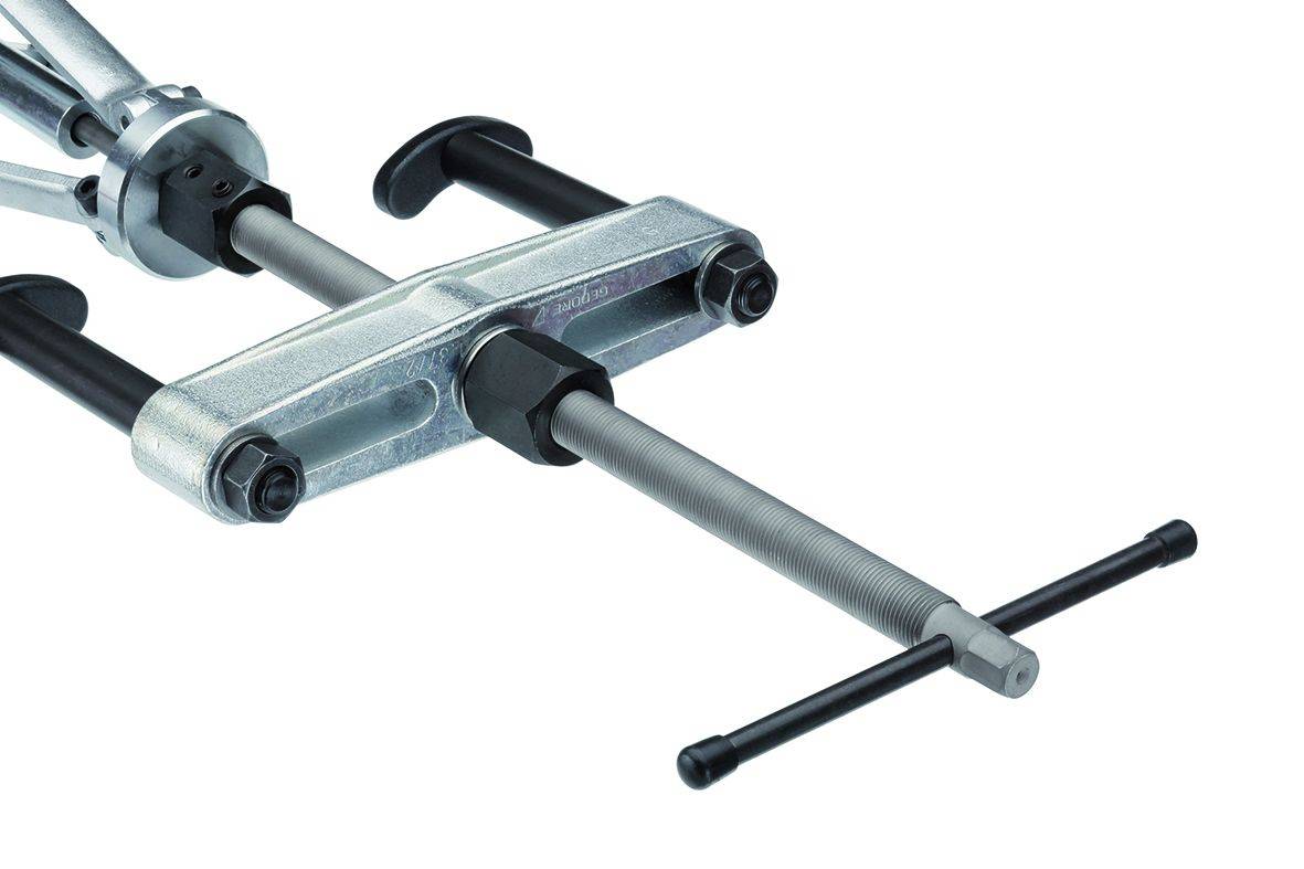 A silver puller or spanner is lying on a white surface. It is used to remove components such as gears or bearings.