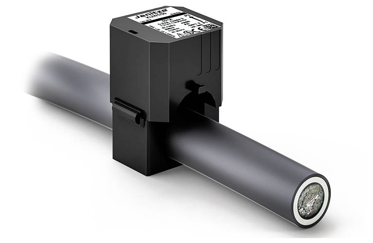 A black sensor is clamped around a thick black cable. It has a label with technical information on its top surface.