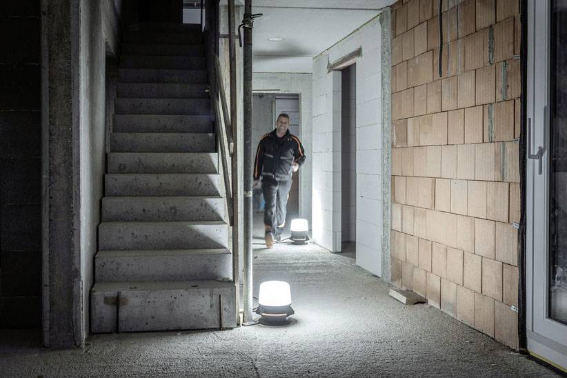 A person is walking through an illuminated, unfinished corridor next to a concrete staircase and a masonry section.