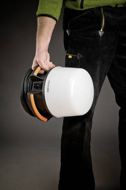 A person is holding a white, helmet-like object with a handle. Suitable for outdoor activities. The person is wearing a green jacket and black trousers.