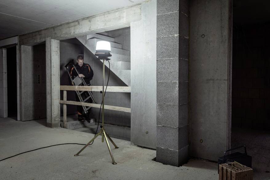 A staircase in an unfinished building. One person is carrying a ladder upstairs. A lamp illuminates the area.