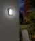 A glowing wall light in a dimmed room, next to a window overlooking an illuminated garden in the evening.