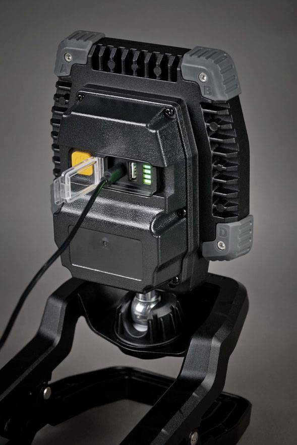 Portable LED floodlight with robust housing, mounted on a tripod. Power cable plugged in, battery status indicator illuminated.