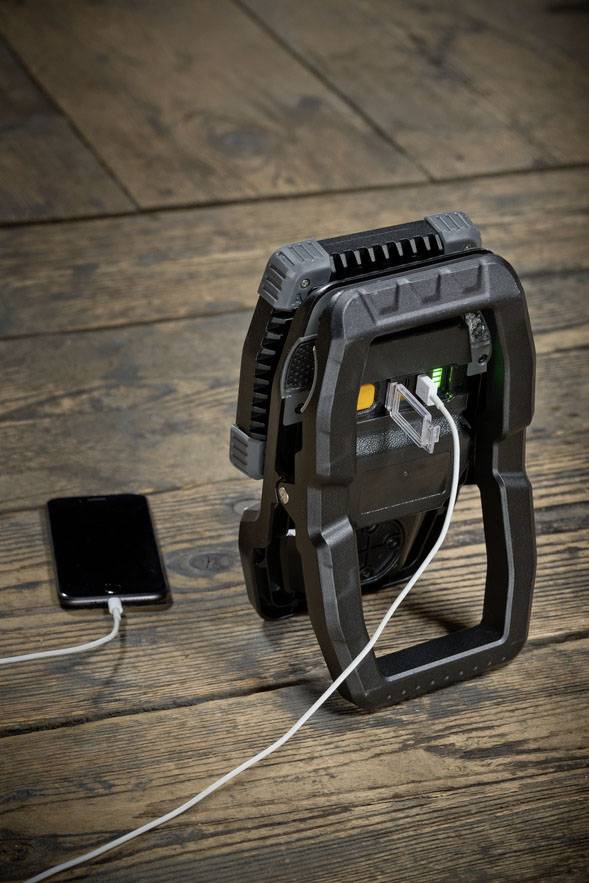 A portable device is charging a smartphone via a USB cable. The device is standing upright on a wooden floor.