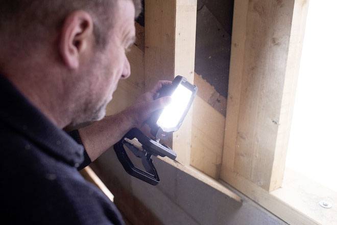 A man illuminates a wooden beam with a torch in an attic, possibly during renovation or construction work.
