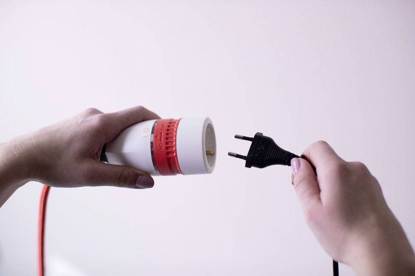 A hand is holding a white, round plug with a red rim. Another hand is holding a black, two-pin plug that is being inserted.