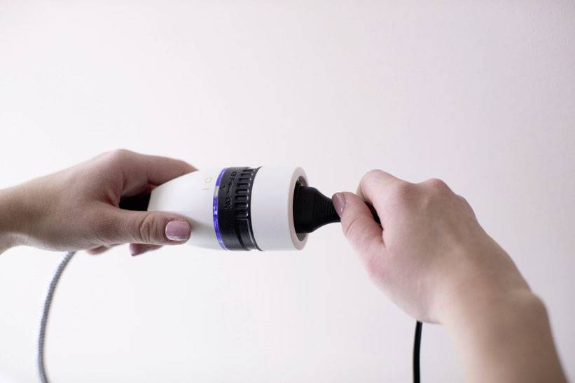 A person is holding a white device with a blue ring and connecting a black cable to it.