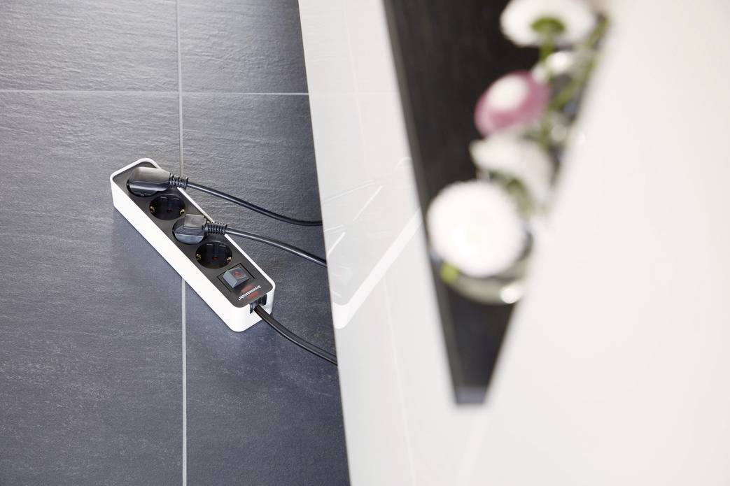 A multi-socket extension lead on a dark floor. It is connected to several cables. The surroundings show parts of a table.