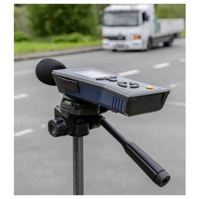 Sound level meter on a tripod by a road, measuring noise from passing traffic with a truck blurred in the background.<br>