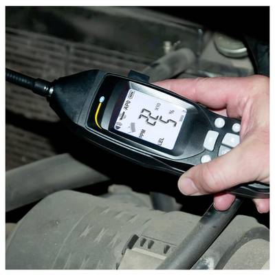Handheld digital air quality meter showing a PM2.5 reading of 22 and 5% battery while held near a vehicle's interior.
