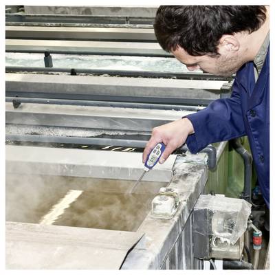 Worker measuring temperature in a steaming industrial tank with a digital probe.