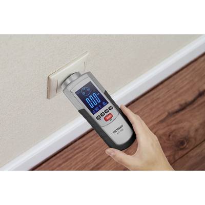 A person is holding an electrical measuring device against a power socket to check the voltage. The display shows 0.00.