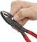'A hand adjusts a black pair of pliers with a red handle, suitable for precise gripping and cutting, on a white surface.'