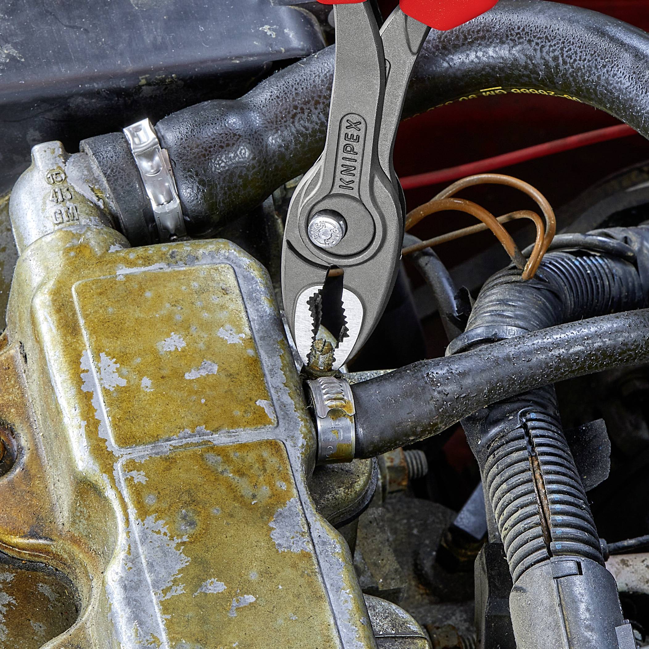 A pair of pliers is holding a rusted component on an old vehicle engine, demonstrating repair or maintenance work.