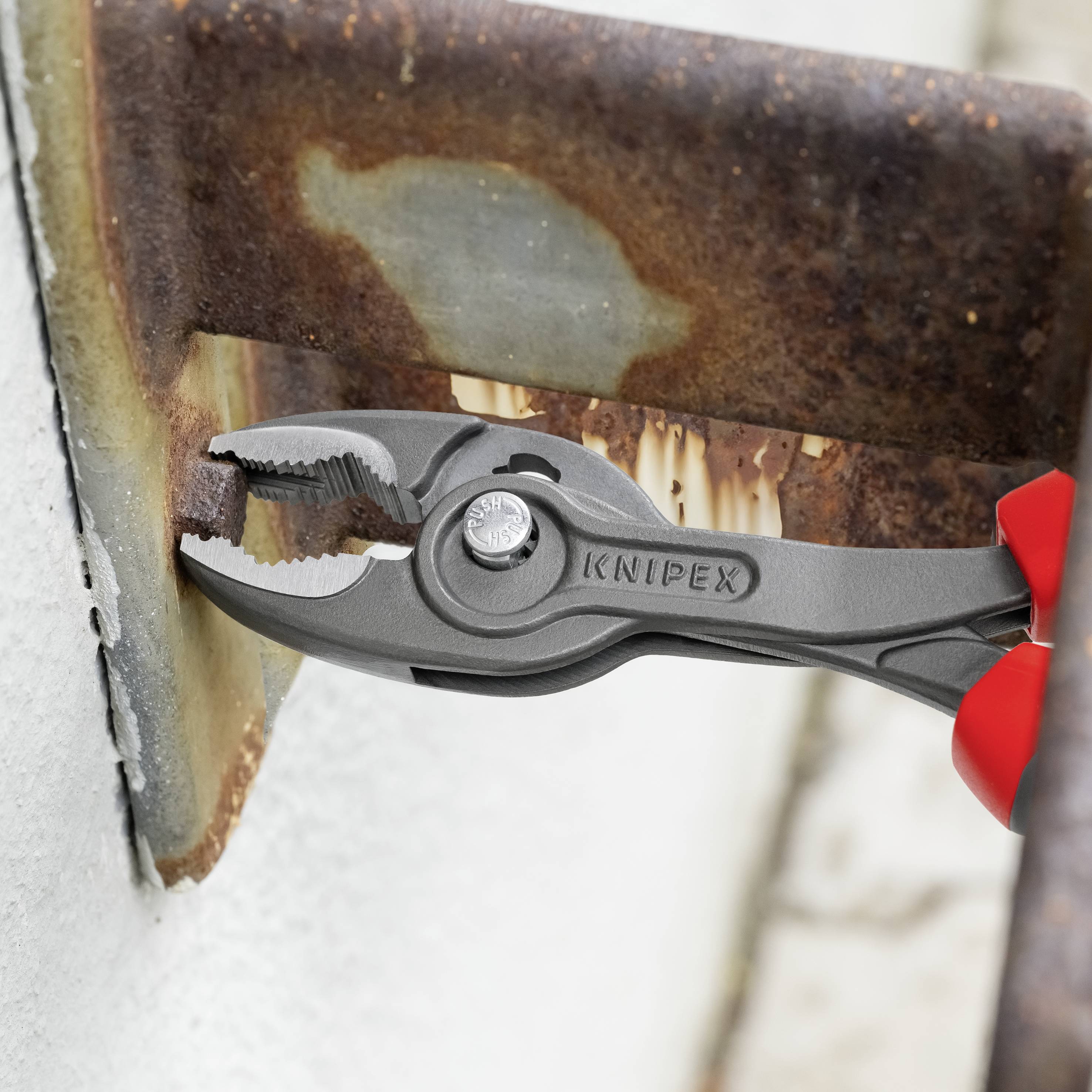A 'Knipex' pliers is gripping a rusty steel part. The red pliers are suitable for loosening screws in difficult-to-reach places.