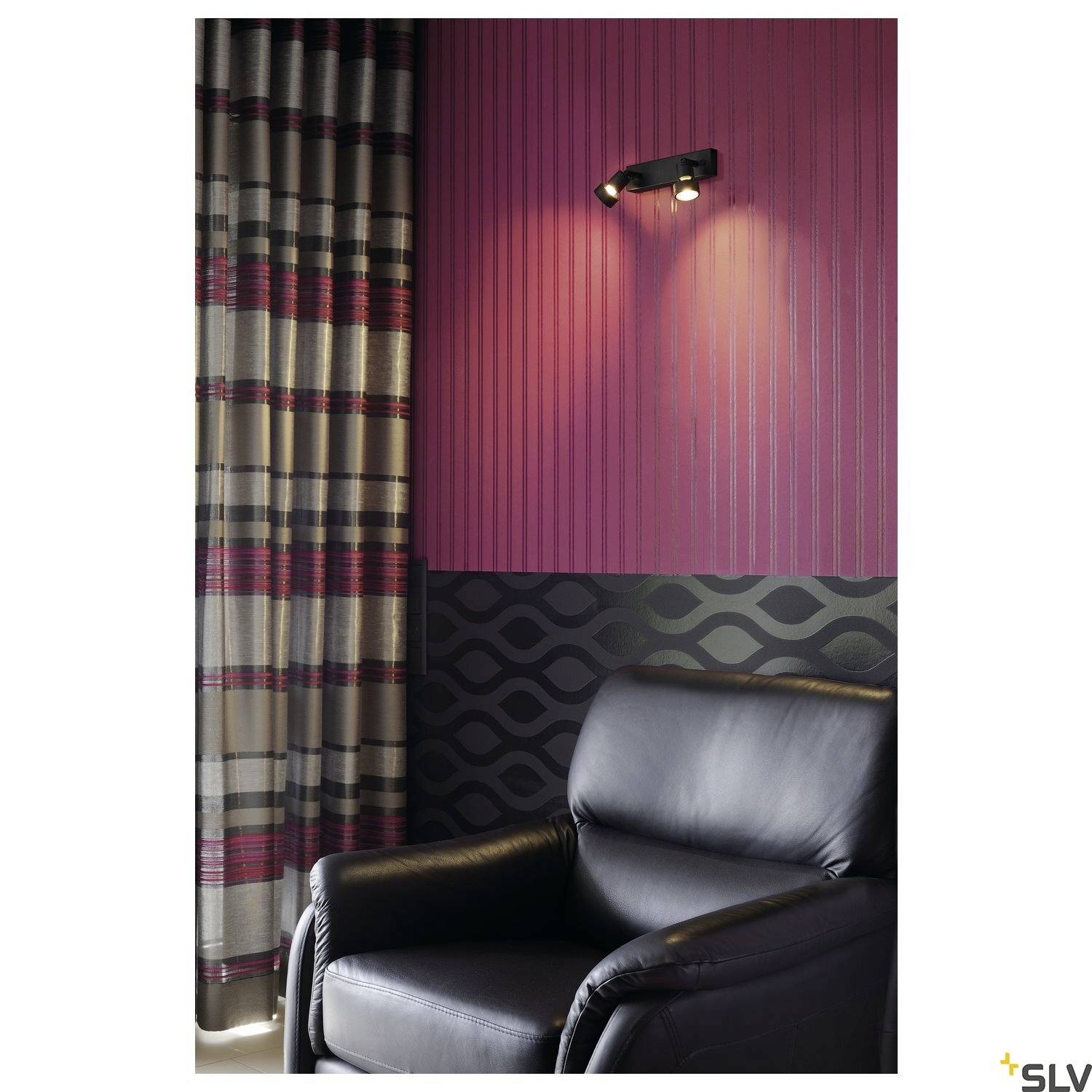 A black leather armchair sits in front of a violet-striped wall with a black pattern. A spotlight is mounted above.