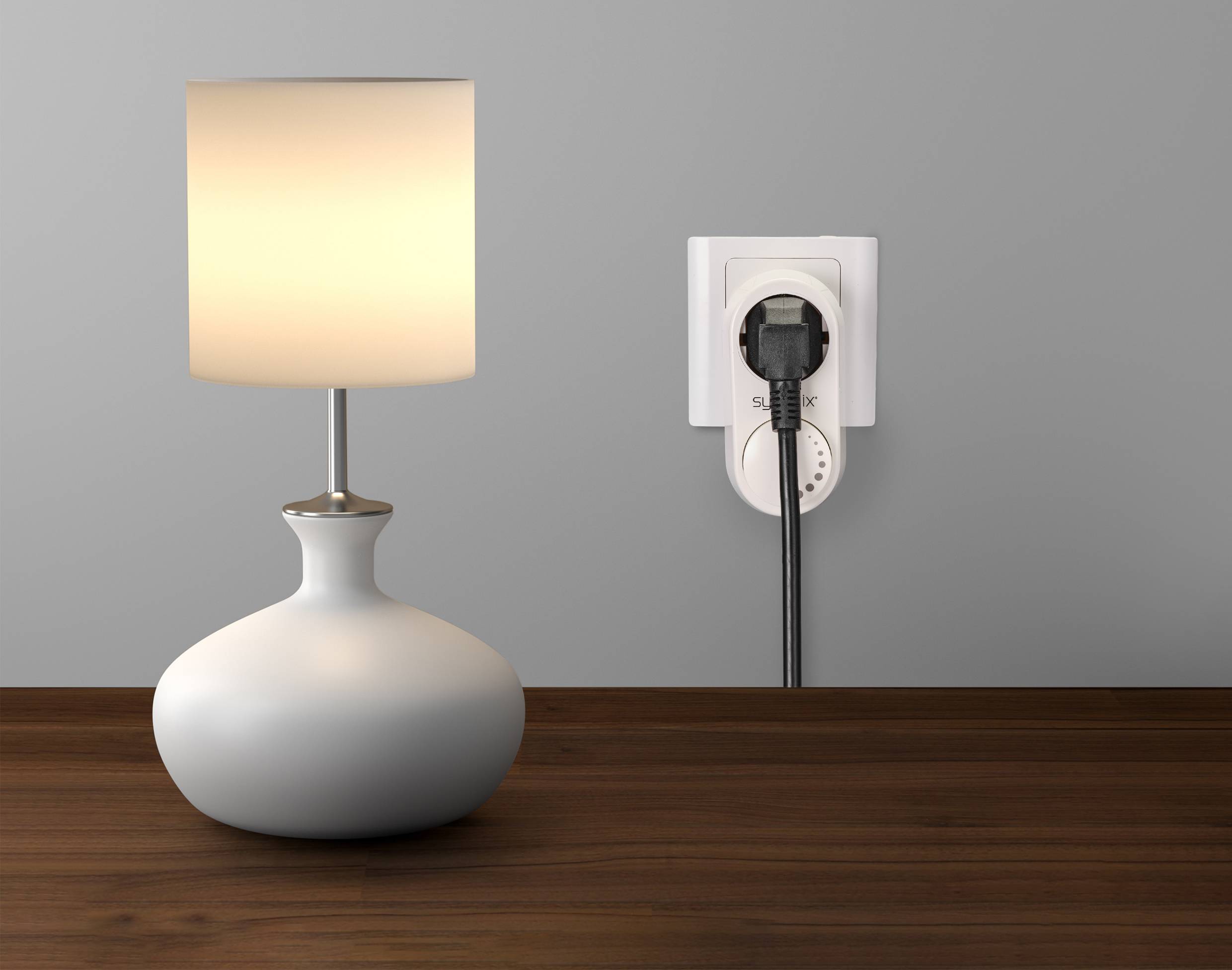 Table lamp with a white lampshade illuminates on a wooden table. Next to it is a power socket with a plug inserted.
