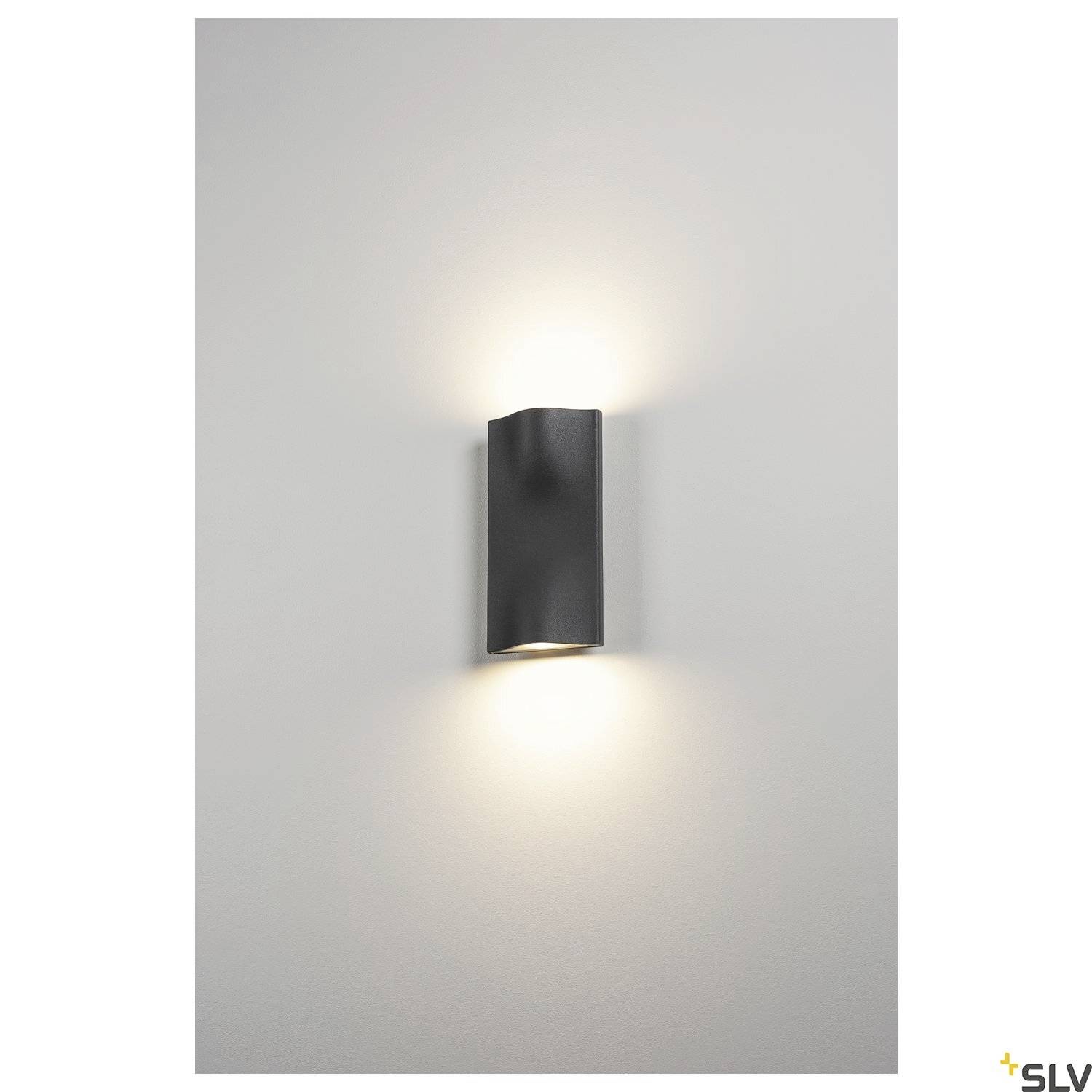 A modern wall light with a cylindrical housing, which radiates soft light upwards and downwards, mounted on a light grey wall.