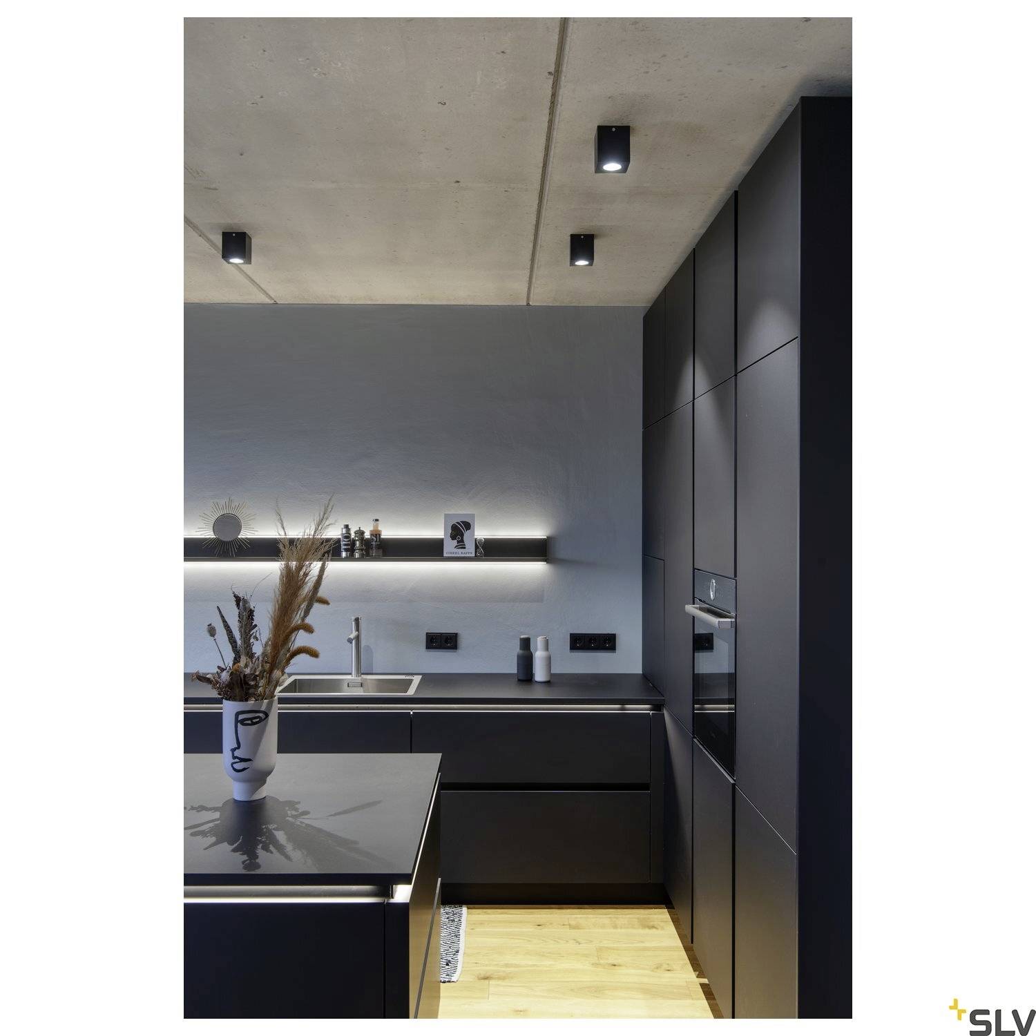 Modern kitchen with dark cupboards and recessed lighting. A vase with dried flowers sits on the worktop.