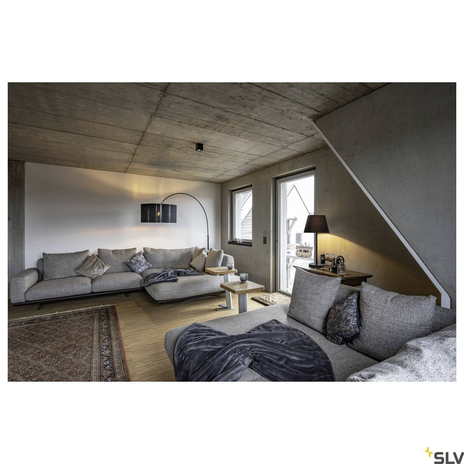 Cosy living room with two grey sofas, a rug, modern standard lamp, and wooden coffee table, with atmospheric lighting.