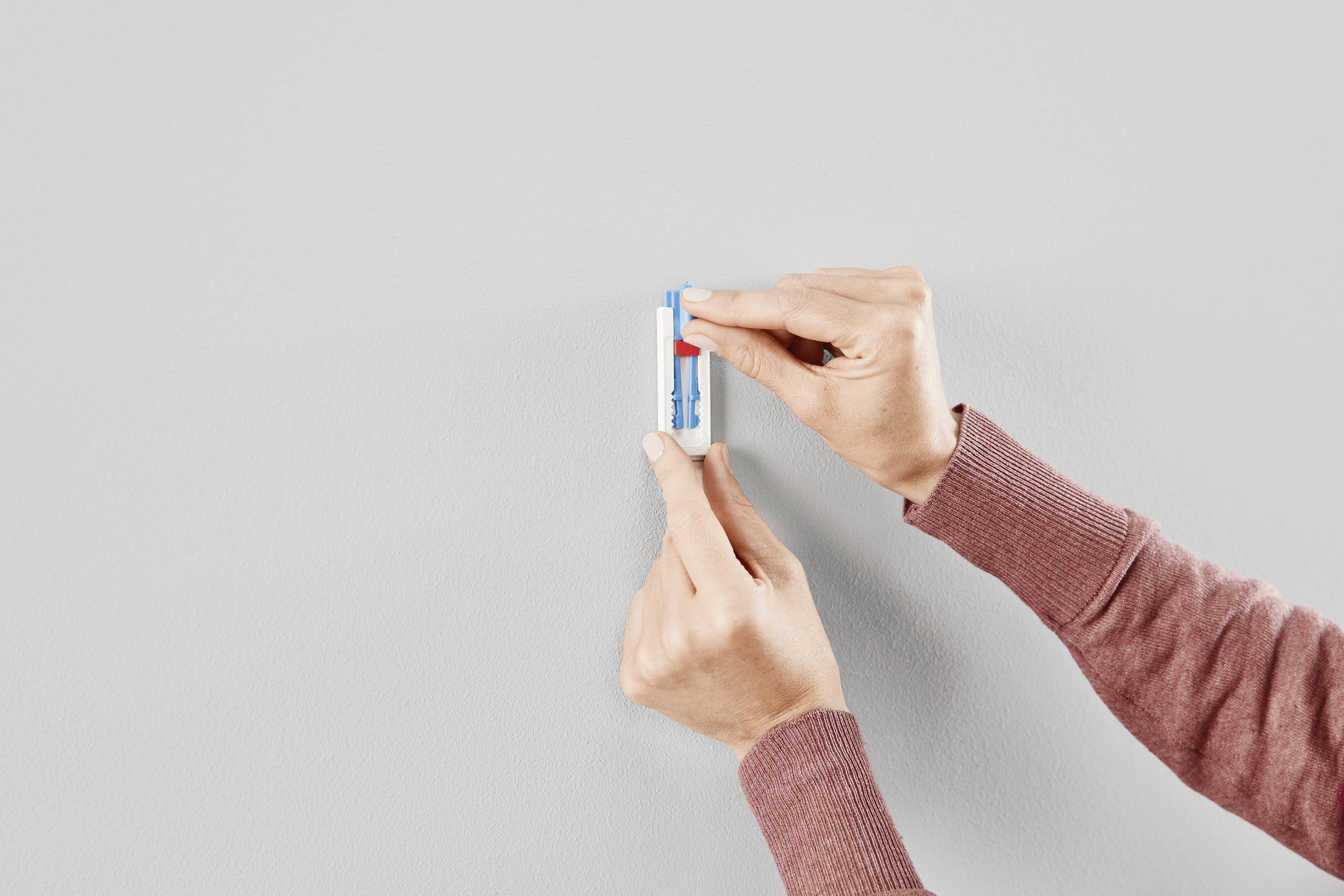 Hands of a person holding a lip balm in a blue and white case against a neutral grey background.