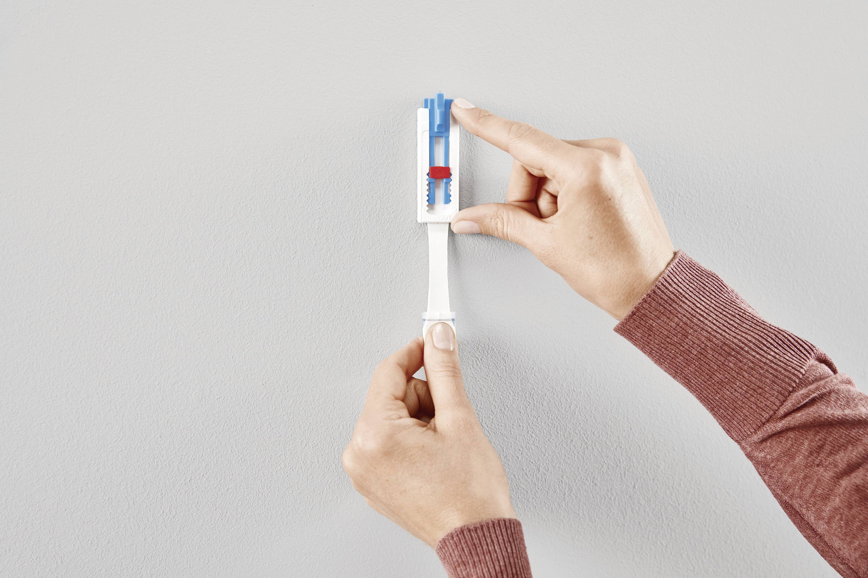 Two hands are mounting a blue and red object onto a white bracket on the wall.