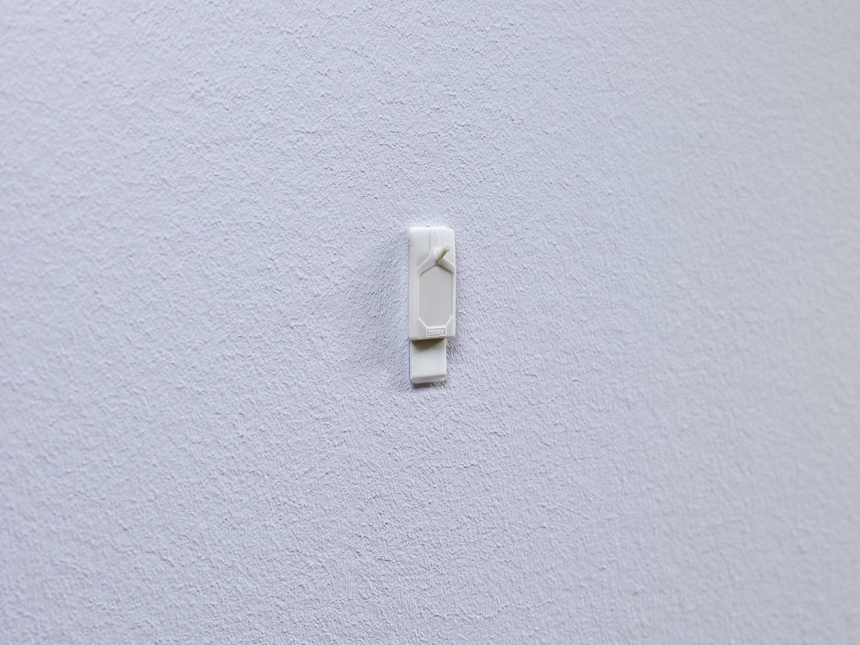 A single white wall hook is mounted on a smooth, white wall.