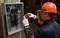 A technician in protective clothing uses a thermal imaging camera to inspect an open fuse box in order to detect electrical issues.
