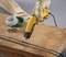 A yellow electrical cable cutter, held by a gloved hand, is cutting cables on a wooden table. Additional cables are lying nearby.