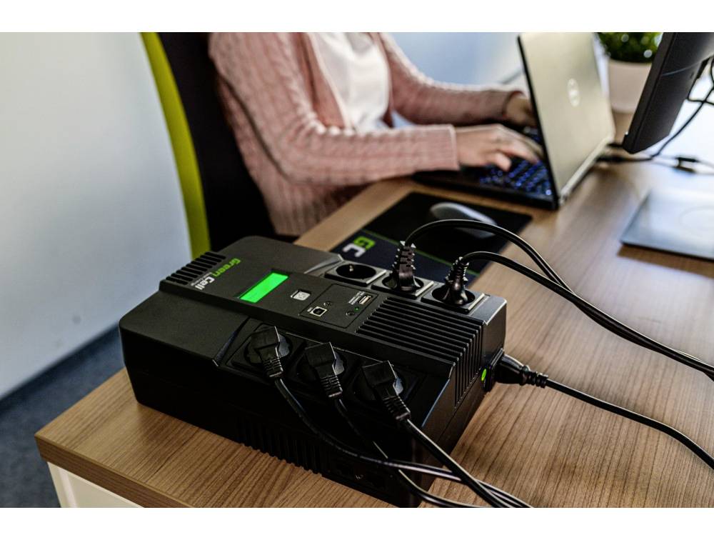 USB device on a table, multiple devices connected. One person with a laptop working in the background, focused on screen work.