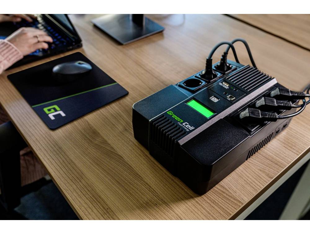 'A person is typing on a keyboard. Next to them, a UPS device with several connected cables sits on a desk.'