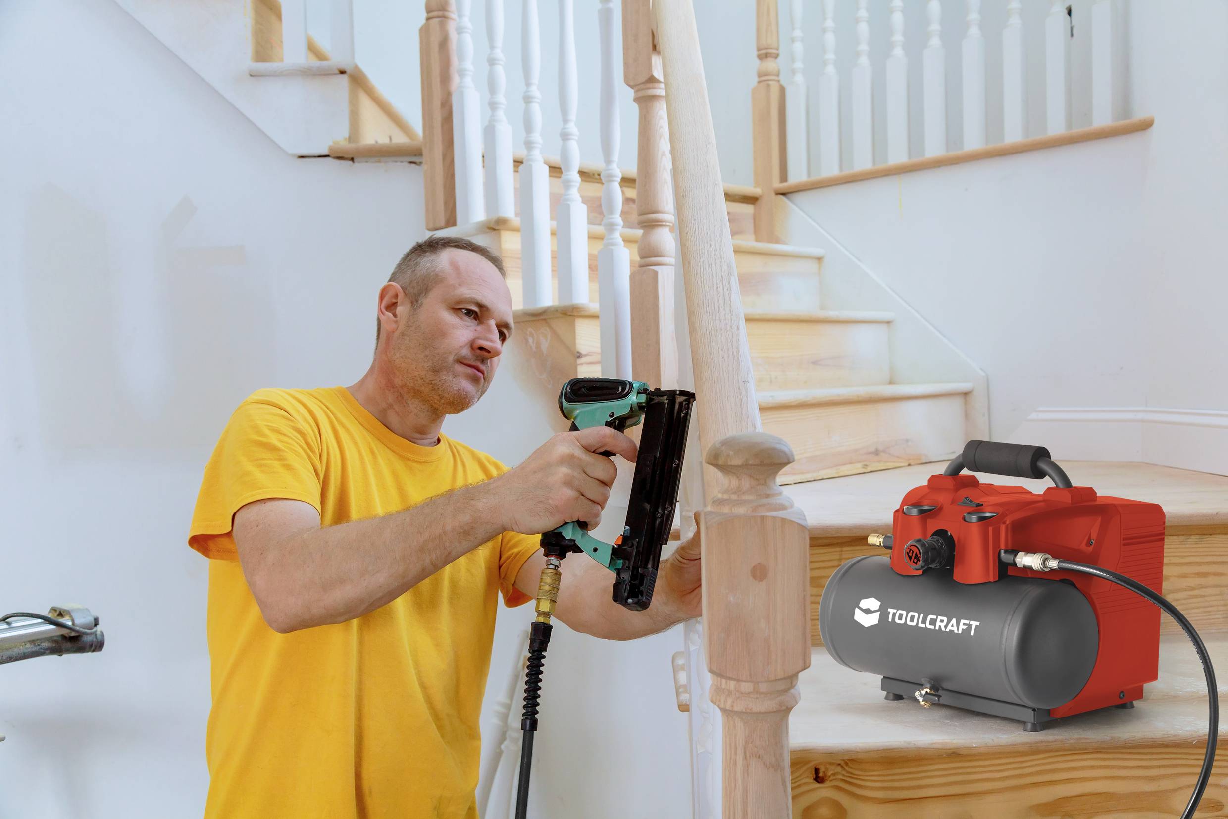 A man in a yellow T-shirt is using a tool to secure wooden bannisters on a staircase. A red air compressor stands nearby.