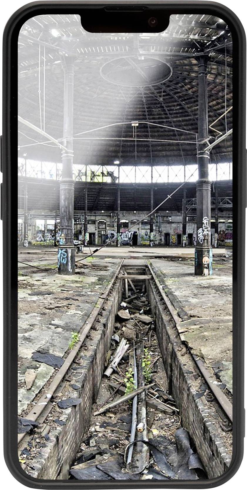 An abandoned factory building with a broken roof and graffiti on the walls, sunlight streaming in. In the foreground, rusty rails and debris.