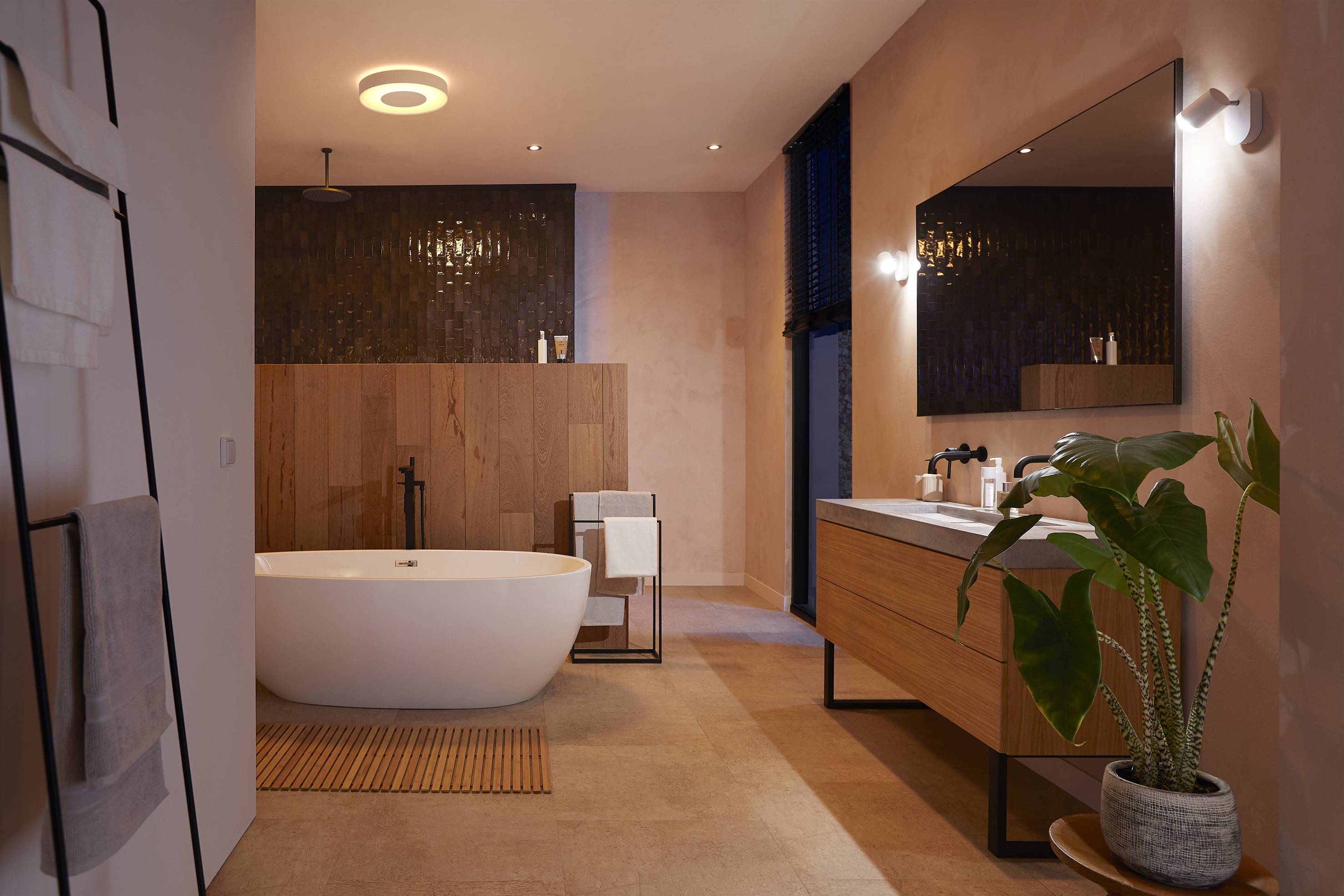 Modern bathroom with a freestanding bath, wooden wall panelling, large mirror, wooden vanity unit and indoor plant.