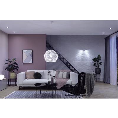 Modern living room with a white sofa, patterned cushions, a geometric pendant light, plants and an abstract painting on the wall.