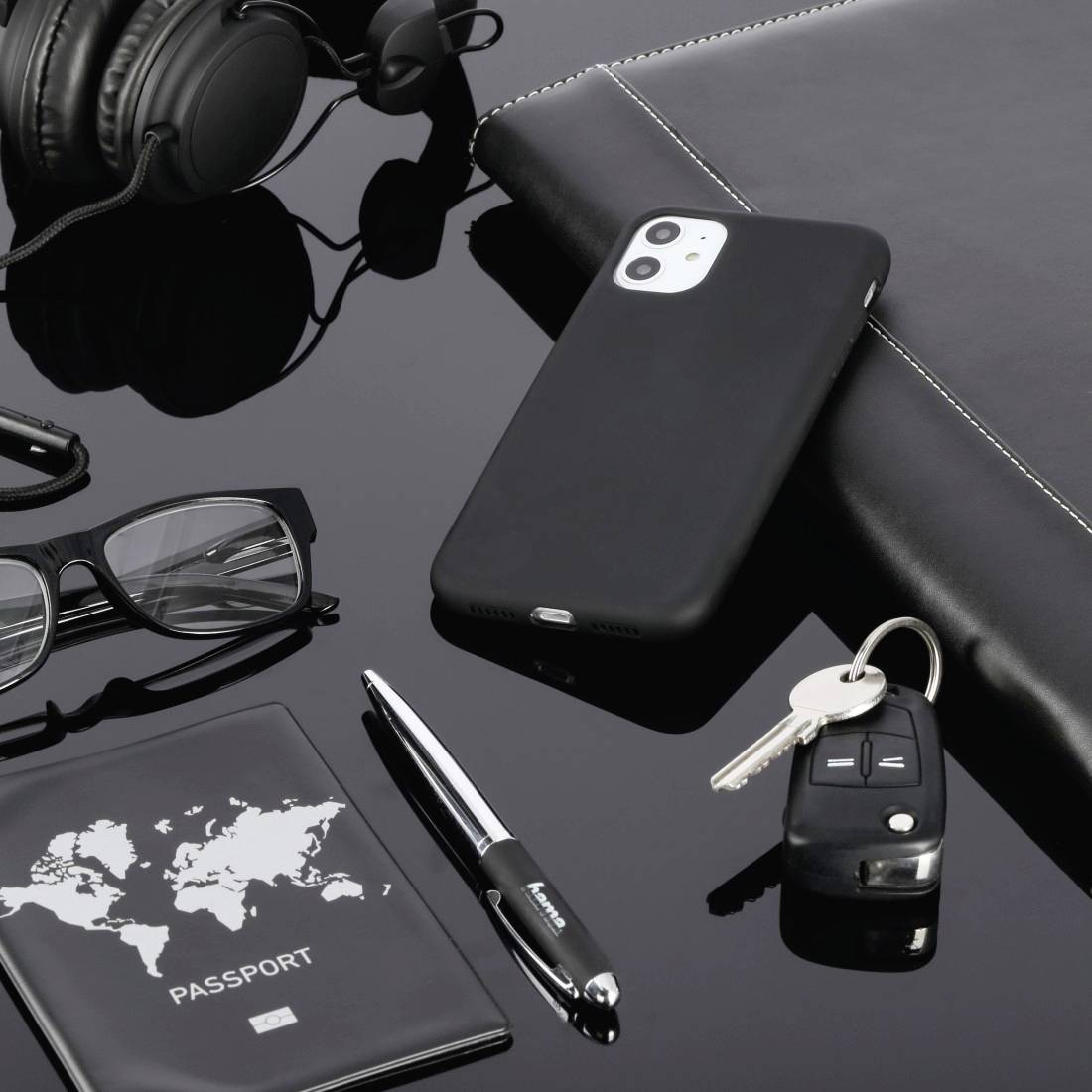Smartphone, headphones, glasses, pen, passport, car keys and notebook on a black surface. Business travel motif.