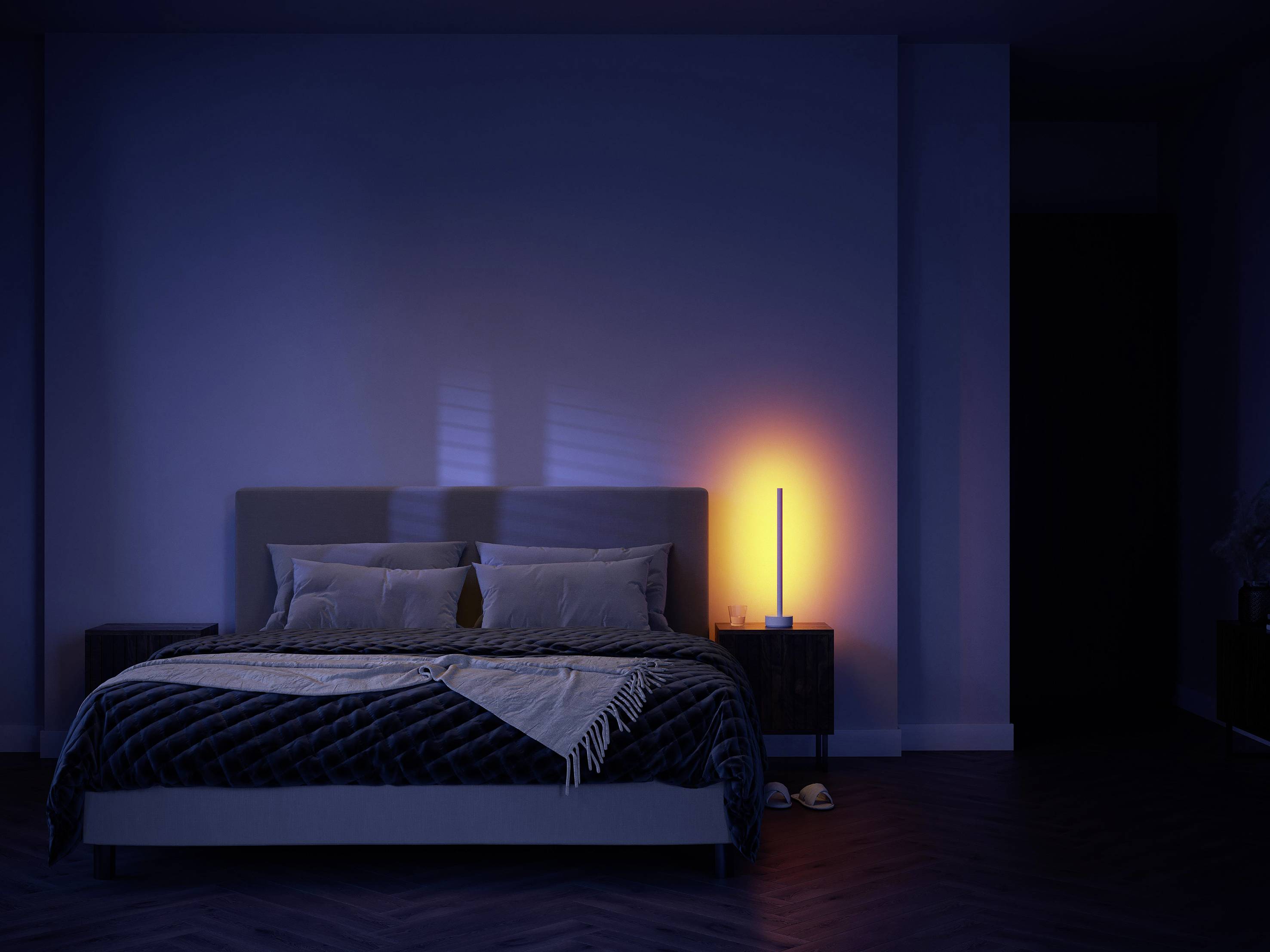Dark bedroom with bedside lamp illuminated on the right side of the bed, casting warm light on a modern, minimalist interior.