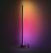 A slender, standing lamp on a round base glows in vibrant colours from pink to orange, creating an atmospheric ambience.