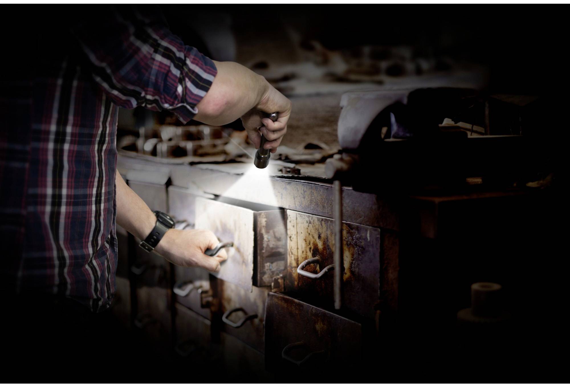 A person is examining an old chest of drawers with a torch in a dark environment.