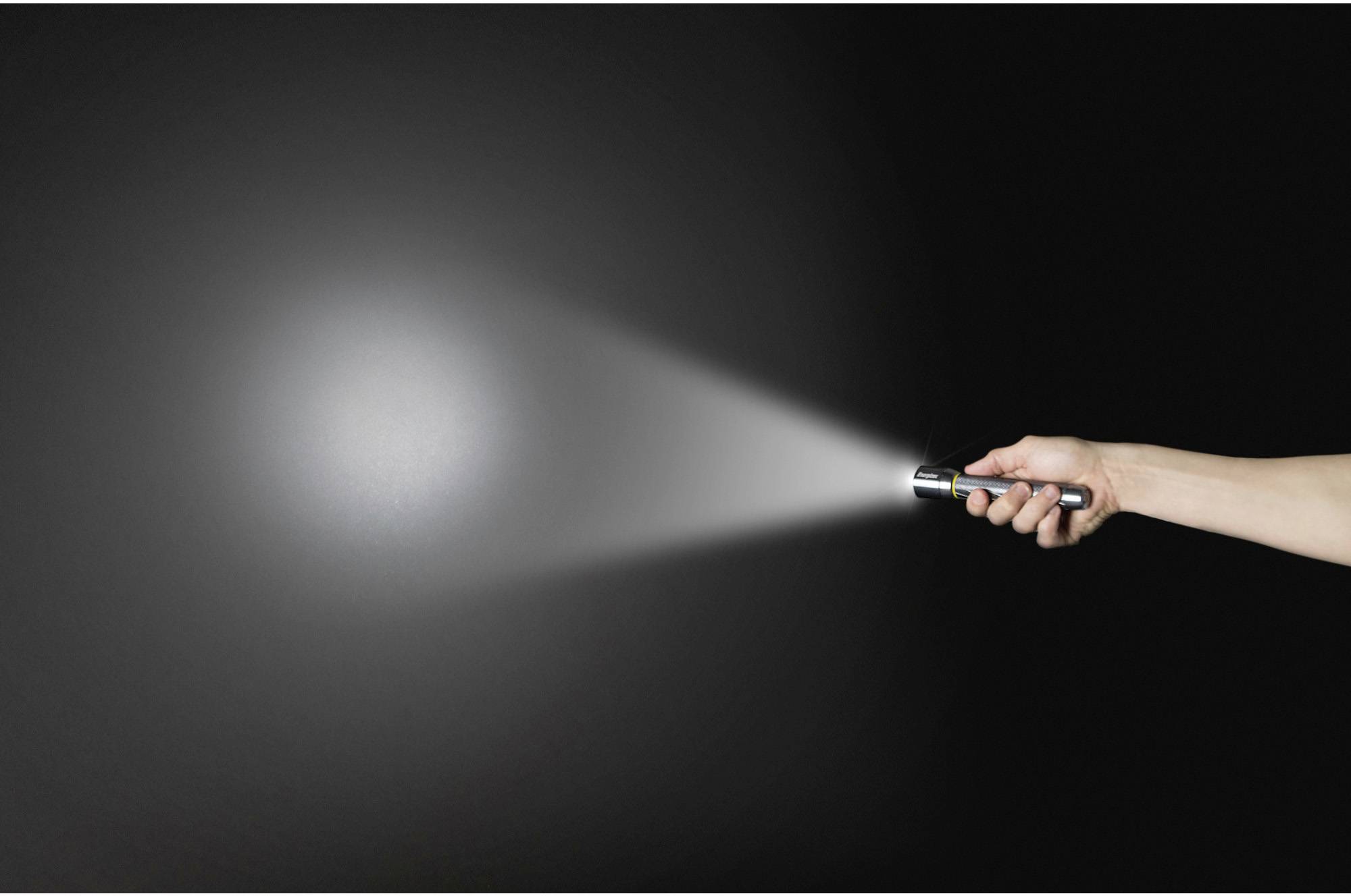 A hand holds a torch in a dark room. The beam of light shines to the right and illuminates a section of the wall.