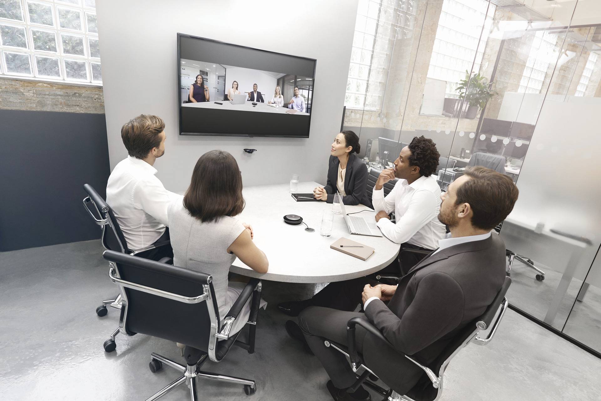 Six people in a conference room are conducting a video meeting. Four people are visible online on the screen.