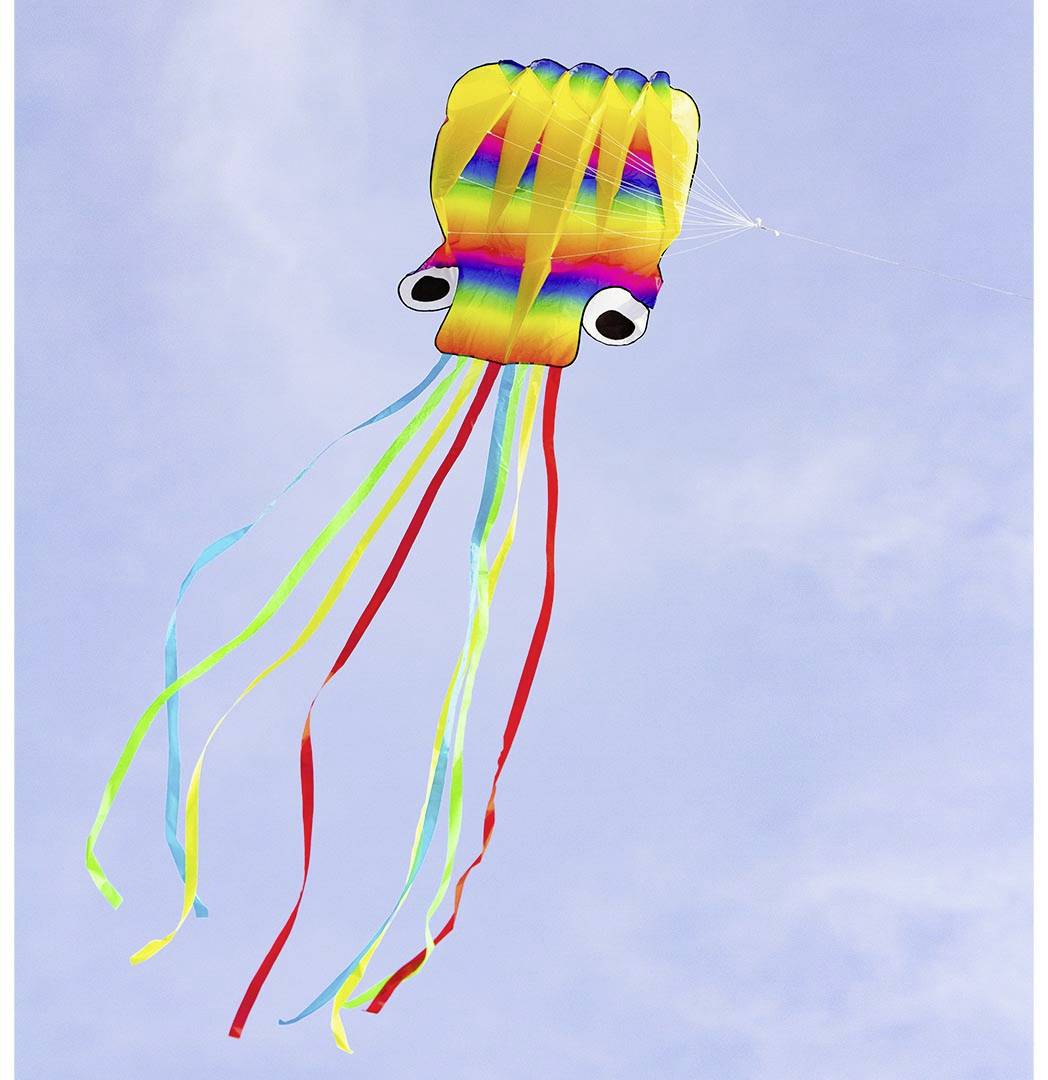 A colourful squid-shaped kite hovers in the blue sky with long, vibrant ribbons fluttering in the wind.