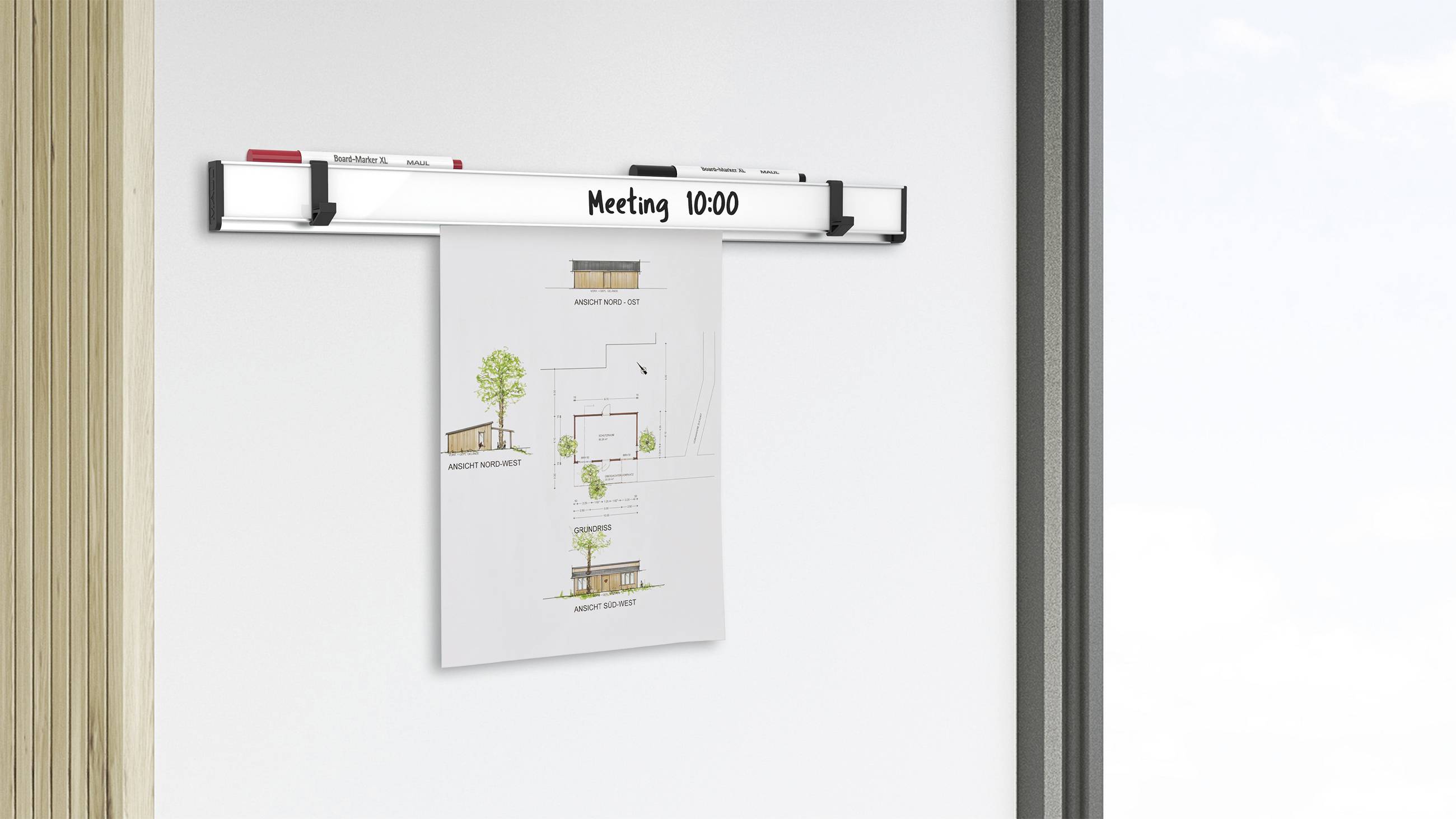 A whiteboard with the inscription 'Meeting 10:00' on a wall, with an architectural design plan hanging underneath.