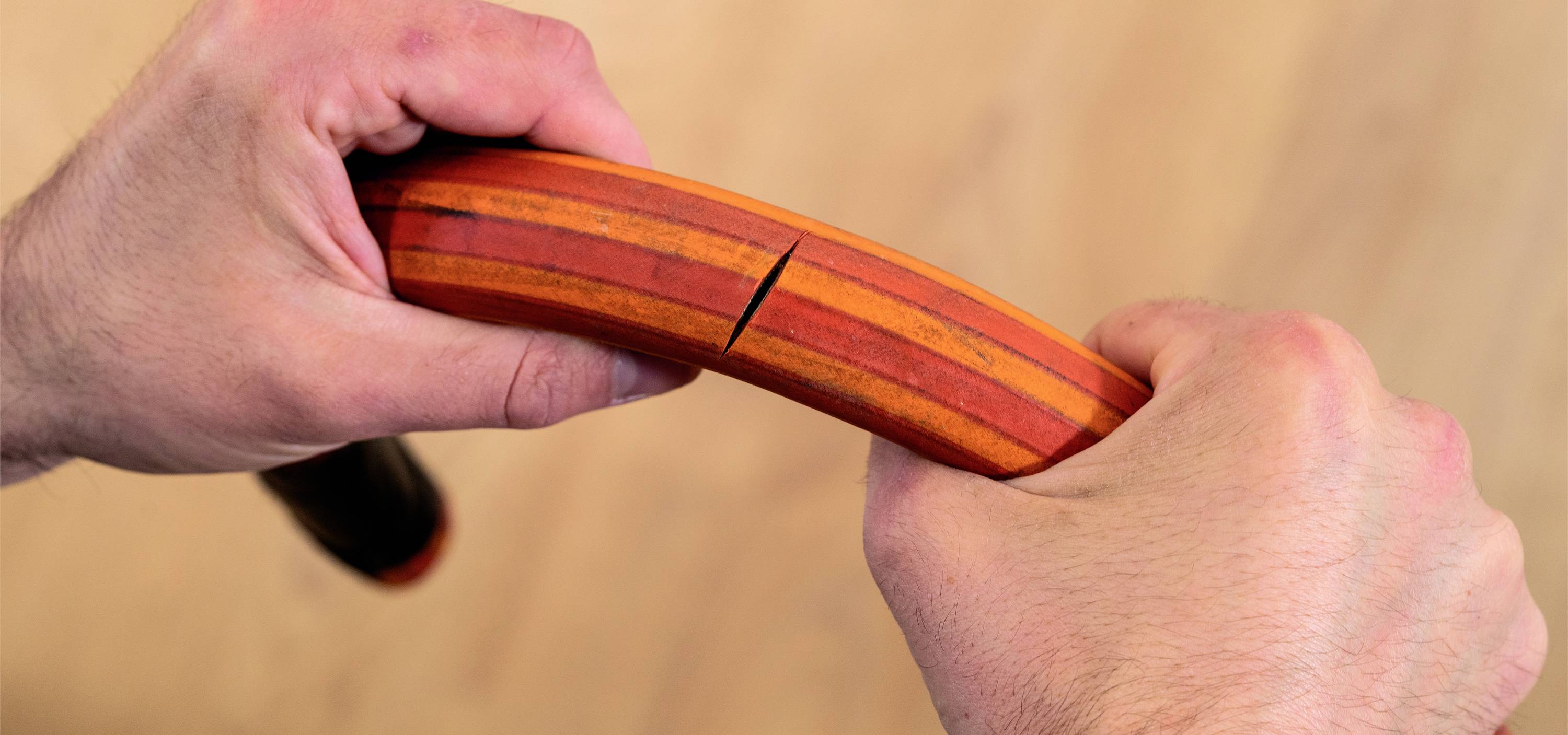 A hand breaks an oval, multi-coloured wooden object. The scene depicts force or exertion. The background is out of focus.