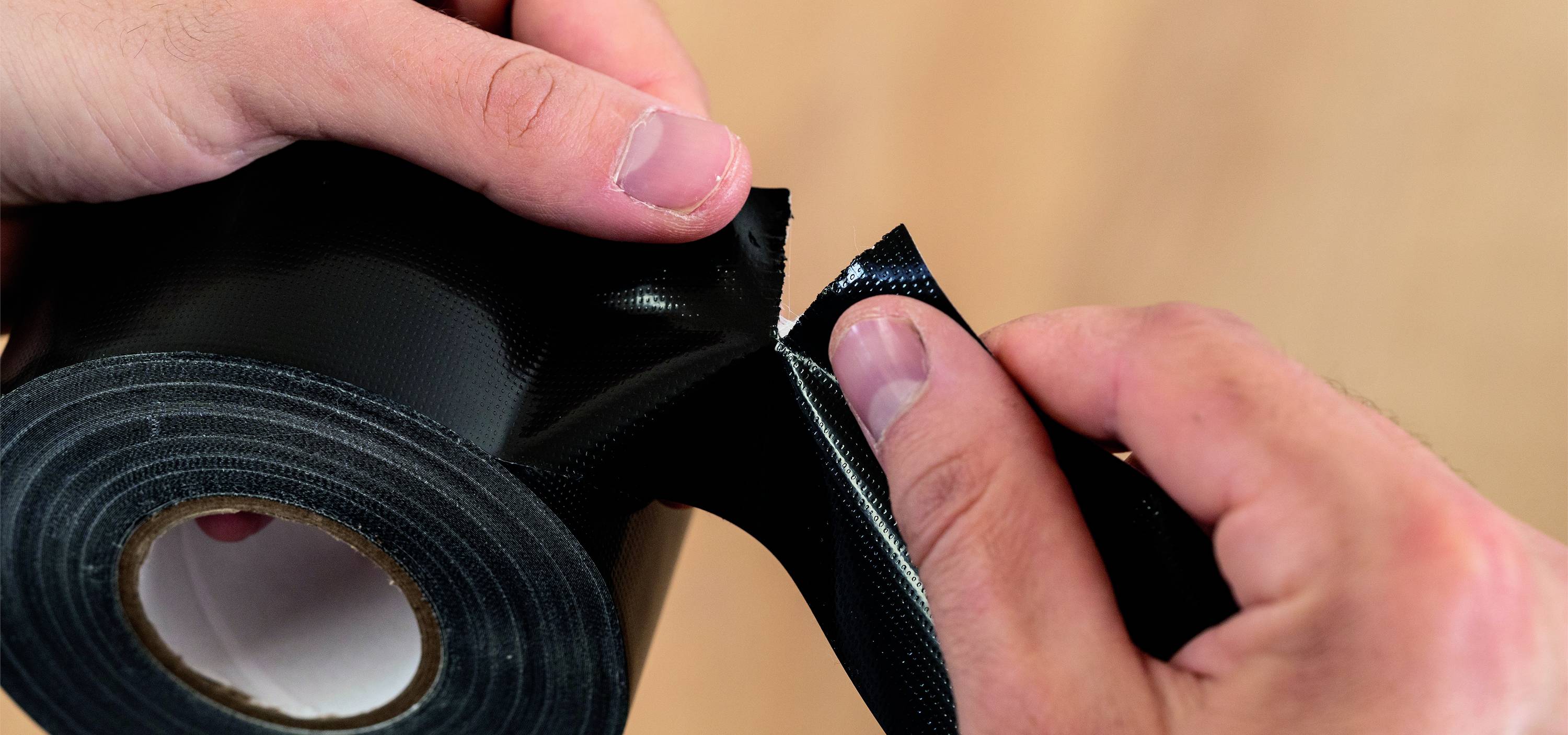 Two hands are separating a piece of black adhesive tape from a roll.