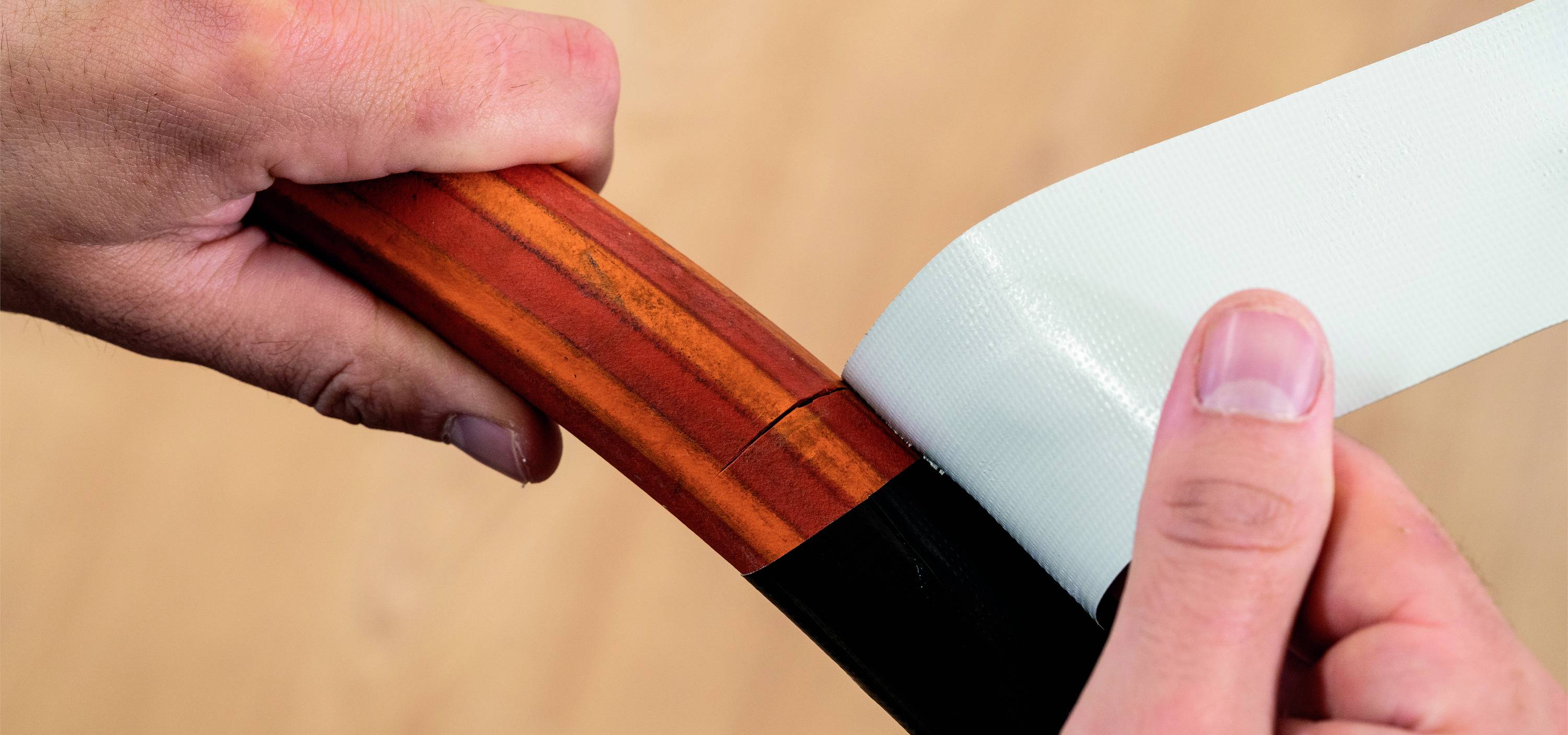 'A person is wrapping a bow with white tape for reinforcement or repair. The bow is dark brown in colour.'