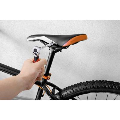 A person is tightening the screws on a bicycle saddle with a spanner. The bicycle has a black frame and chunky tyres.